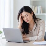 パソコン作業中に頭痛で顔をしかめる女性