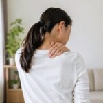 首から肩にかけて手を当てている女性